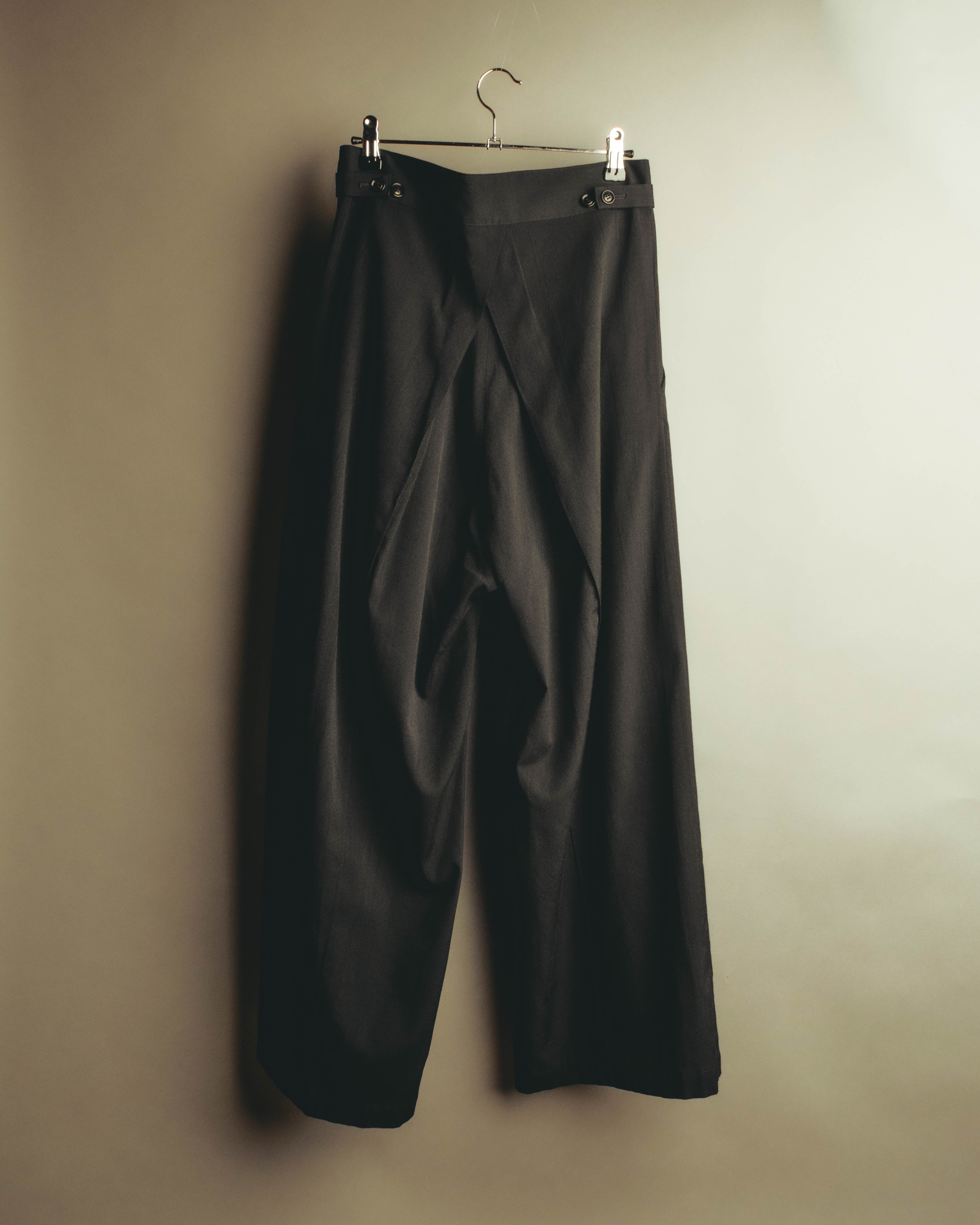 ブラックのワイドストレートシルエットを前面から捉えた全体カット。ウエスト両脇のボタン式アジャスターと、腰回りにゆとりを生むフロントタックが確認できます。