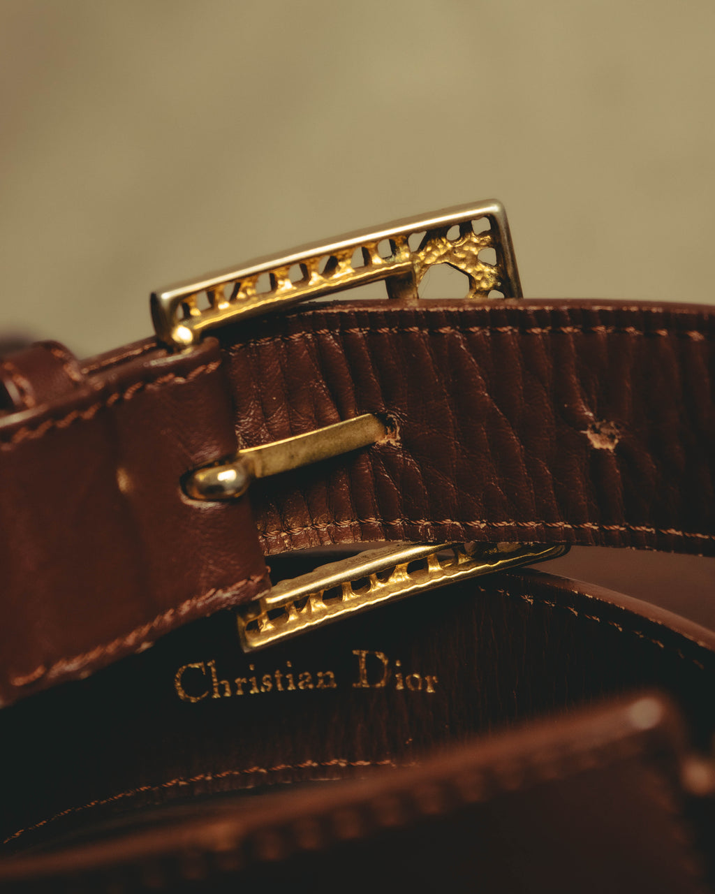 ゴールド調の透かしバックル裏側に配されたピン式の留め具と、帯材内側のセリフ体「Christian Dior」金色箔押し表記を捉えたディテールカット。帯材の細かなシボと端正なステッチ、箔押しの薄れも確認できます。