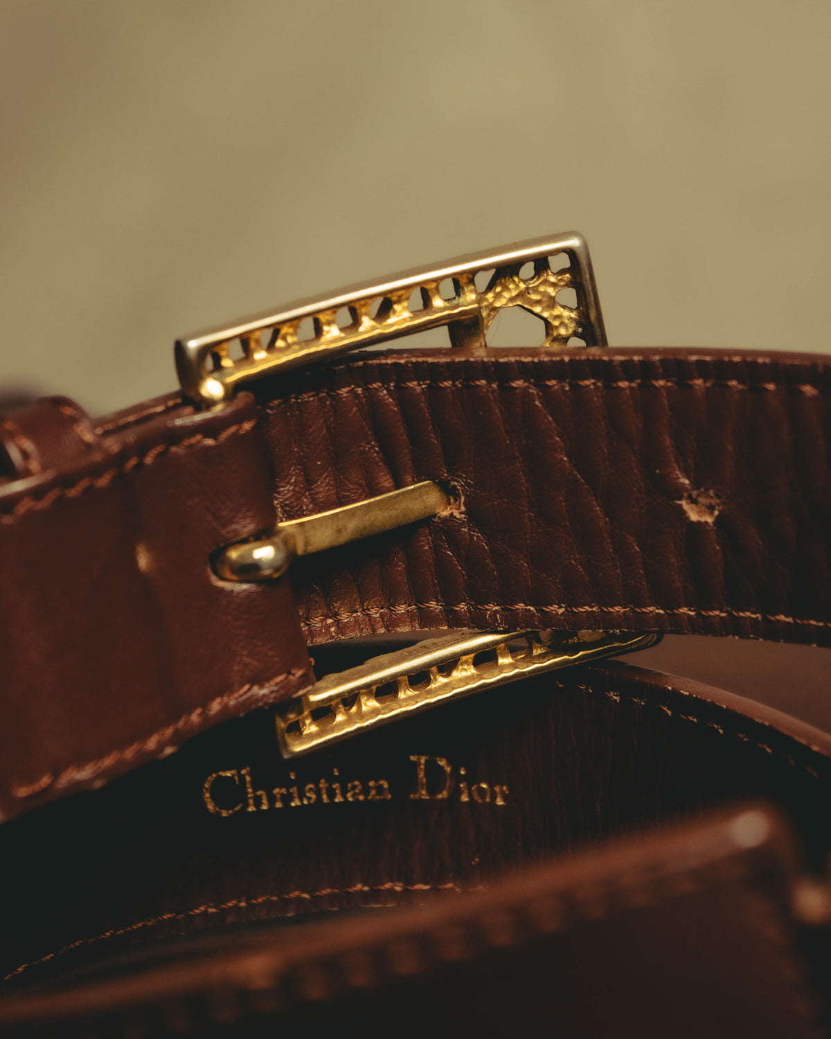 ゴールド調の透かしバックル裏側に配されたピン式の留め具と、帯材内側のセリフ体「Christian Dior」金色箔押し表記を捉えたディテールカット。帯材の細かなシボと端正なステッチ、箔押しの薄れも確認できます。