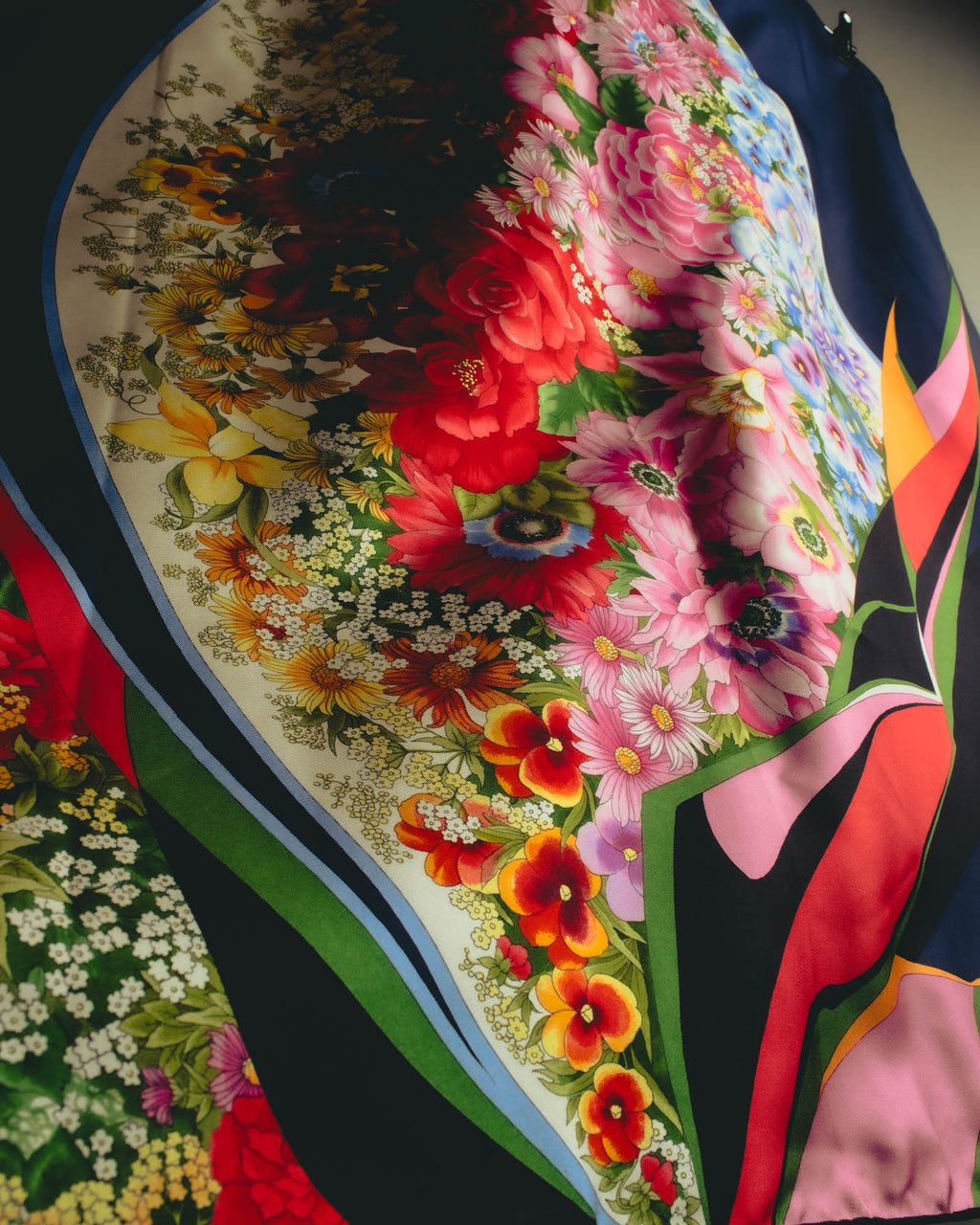 クリームからアイボリーの区画に、レッドやピンク、ライトブルー、イエローなどの花々を密に描いた柄のディテール。ネイビー地と直線的なフレーム、幾何学的な帯がフローラル柄を囲みます。