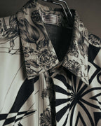 白系の織り地に黒い二重枠を配したVERSUS Gianni Versaceの旧形式ラベルと、線描の花柄を配した襟元を捉えたカット。身頃にはモノトーンのオプティカルパターンが続く。