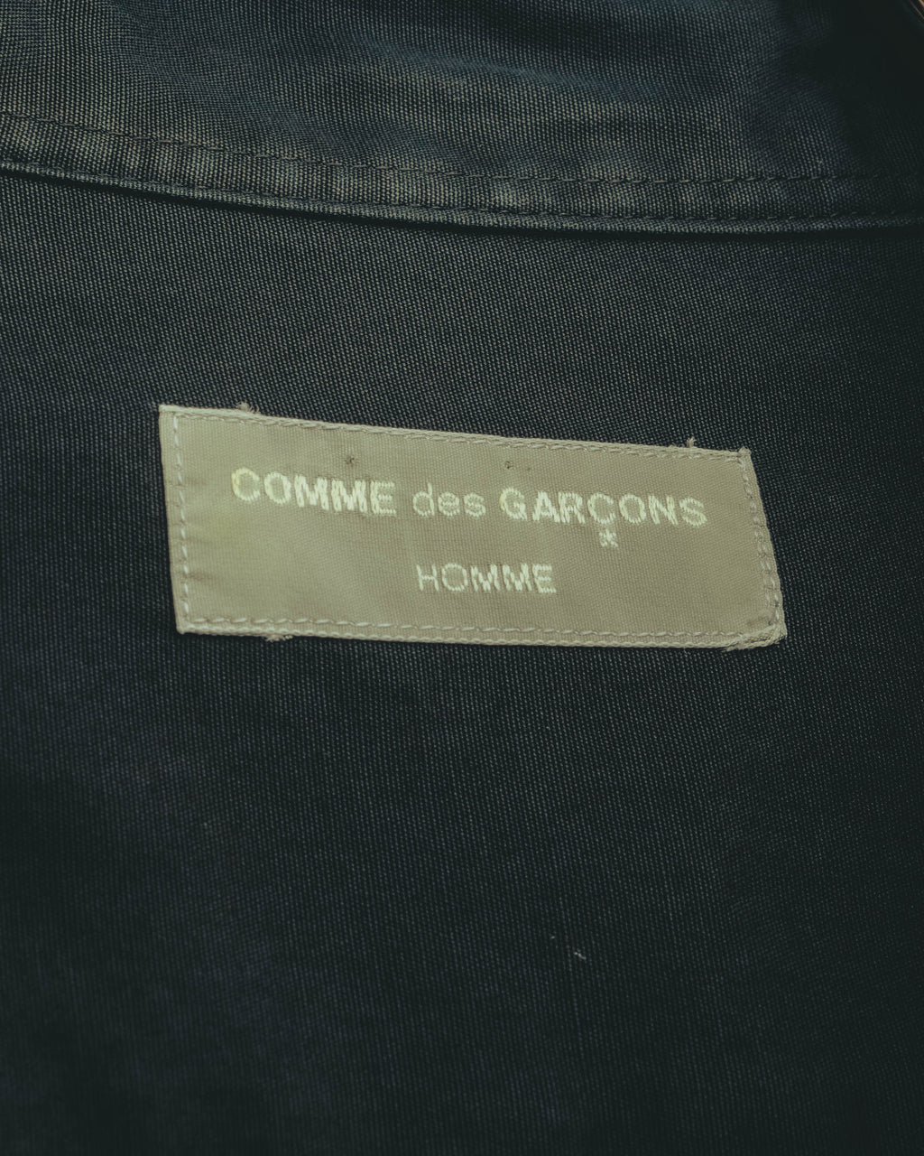 グレーからオリーブを思わせる織りテープに、白文字で「COMME des GARÇONS HOMME」を配したネックタグのクローズアップ。
