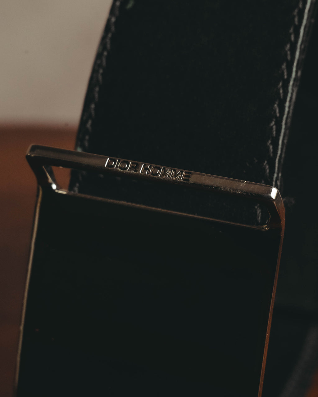 鏡面仕上げのプレートバックル上部に配された、DIOR HOMME刻印のディテールカット。ブラックのベルト本体と両端のステッチも確認できます。