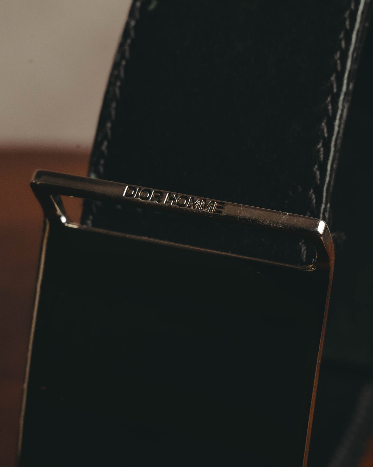 鏡面仕上げのプレートバックル上部に配された、DIOR HOMME刻印のディテールカット。ブラックのベルト本体と両端のステッチも確認できます。