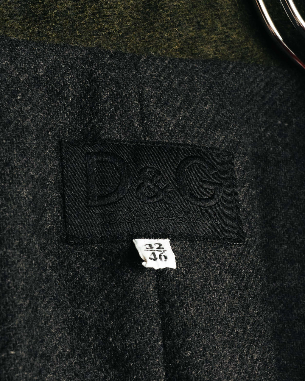 襟元に配されたD&G DOLCE & GABBANAのブランドタグと、32／46表記のサイズタグを捉えたカット。内側のウール混生地の繊細な起毛感も確認できます。