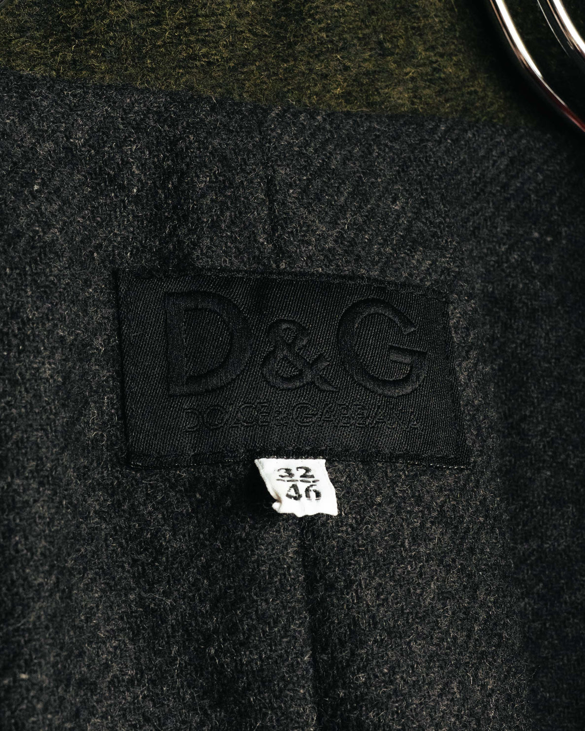 襟元に配されたD&G DOLCE & GABBANAのブランドタグと、32／46表記のサイズタグを捉えたカット。内側のウール混生地の繊細な起毛感も確認できます。