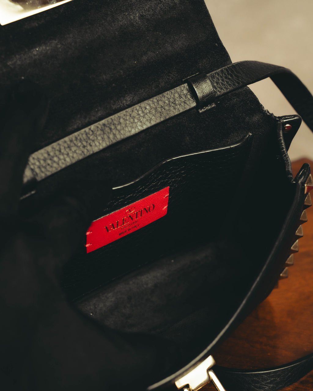 ブラックのスエードタッチの内装に配された、Vロゴとブランドネーム、MADE IN ITALYの箔押し入りレッドレザーパッチのディテール。開口部脇には外周へ連なるピラミッド型スタッズも確認できます。
