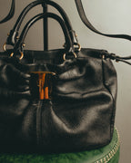 中央に筆記体のFerragamoロゴを刻んだ大型のゴールドトーン留め具（クラスプ）と、丸環でつながるトップハンドルを捉えたフロントディテール。深いギャザーを寄せたブラックレザーボディも確認できるカット。