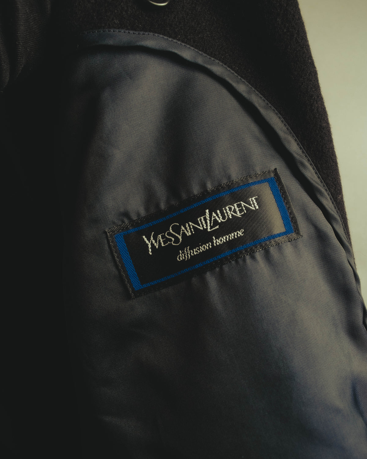 総裏仕立ての内側に配された「Yves Saint Laurent diffusion homme」のブランドタグ。黒地にブルーの縁取りを施した織りネームです。