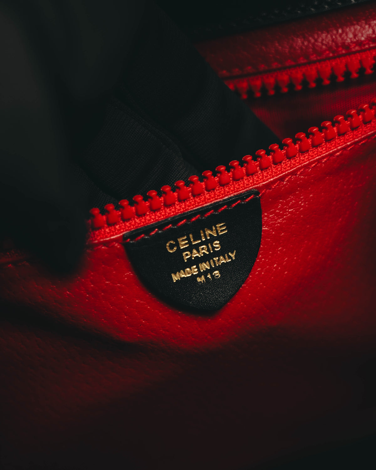 鮮烈なレッドの内装に、CELINE PARIS MADE IN ITALY M 13と金色で刻印された黒色の内タグを配したカット。内装ポケット上部には同色の大型樹脂エレメントファスナーが確認できます。