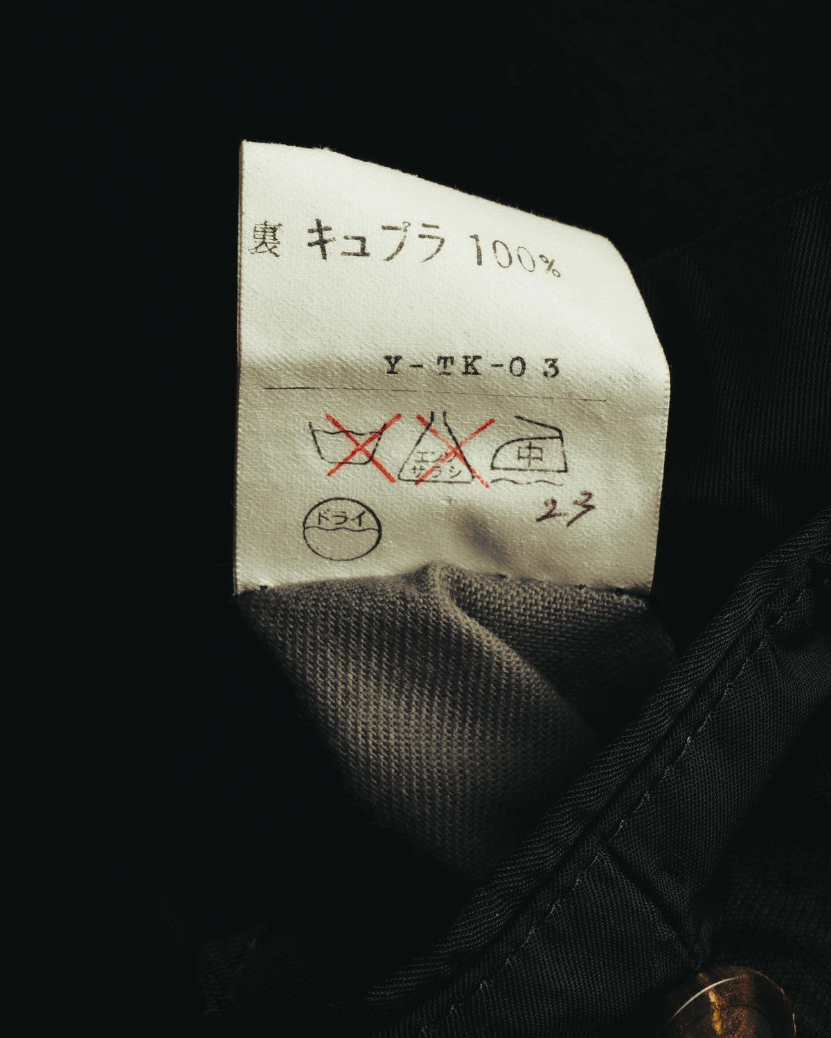 裏地側に配された品質表示タグのクローズアップ。表地が「毛 キュプラ 100%」と記載され、洗濯表示と品番表記を確認できるカット。