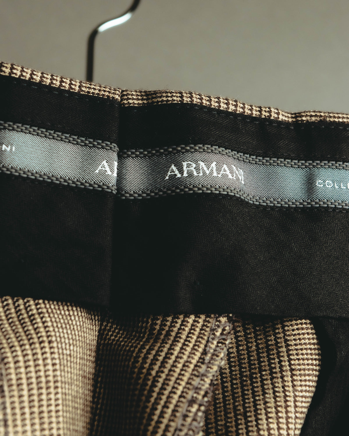 ジャケット内側に配されたARMANI COLLEZIONIのブランドタグと、落ち着いたブラウンの裏地を捉えたカット。襟元にはブラウンからトープを基調とするグレンチェック生地が確認できます。