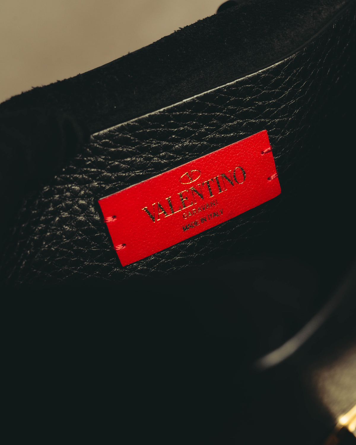 ブラックの内装に配された鮮やかなレッドのレザーパッチ。楕円形のVロゴ、VALENTINO GARAVANI、MADE IN ITALYの箔押しを確認できるタグカット。