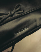 同色のリボンを配したフラップ中央から、前面下部のBALENCIAGA型押しロゴまでを捉えたディテールカット。サテン系素材の繊細な表情と縁のステッチも確認できます。