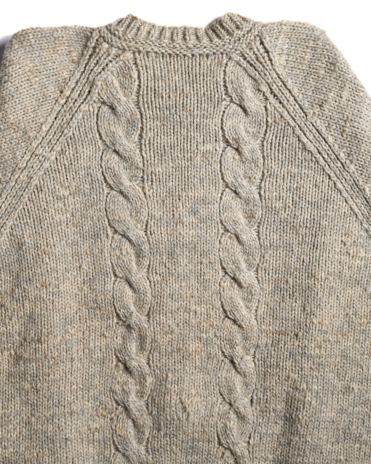 背面に配置された2本のケーブル編みを中心に捉えたディテールカット。首元のしっかりと編み込まれたラウンドネックと、メランジ調ベージュの天竺編みも確認できます。