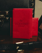 ブラックの内装に配された、VロゴとVALENTINO GARAVANIの表記を備える鮮やかなレッドのレザーパッチ。周囲にはフリップロックとピラミッド型スタッズ、細身のショルダーストラップも写ります。