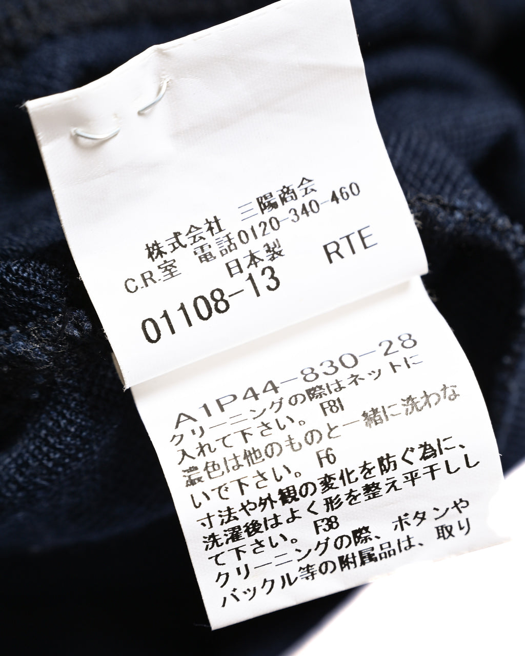 ネイビーニットの内側に付属する品質表示・ケアタグのクローズアップ。クリーニング時の注意書きと品番表記が確認できるカット。