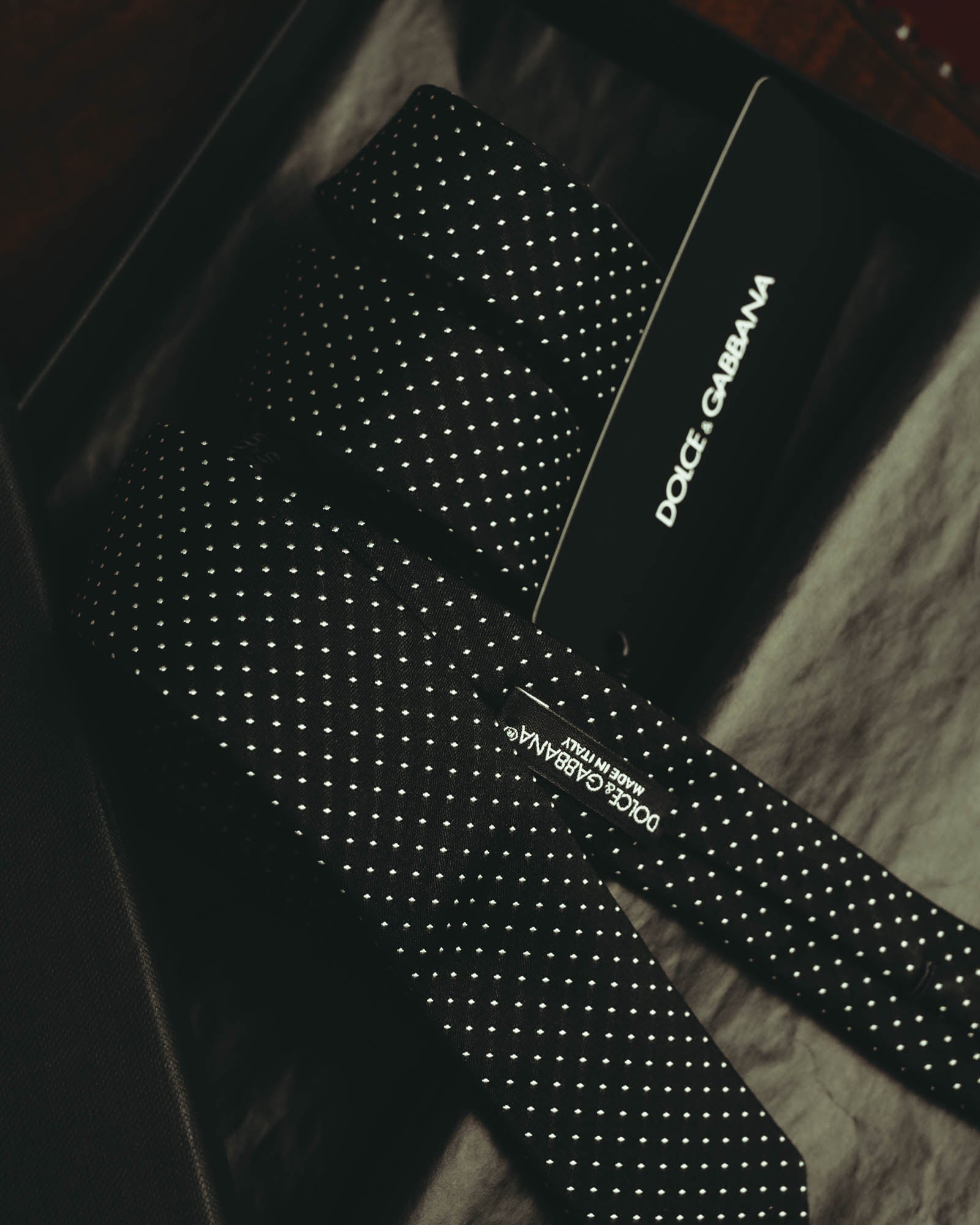 ブラックを基調にホワイト系の極小ドットを規則正しく配した、細身ネクタイの全体を捉えたカット。ブランドタグと「MADE IN ITALY」表記も確認できます。