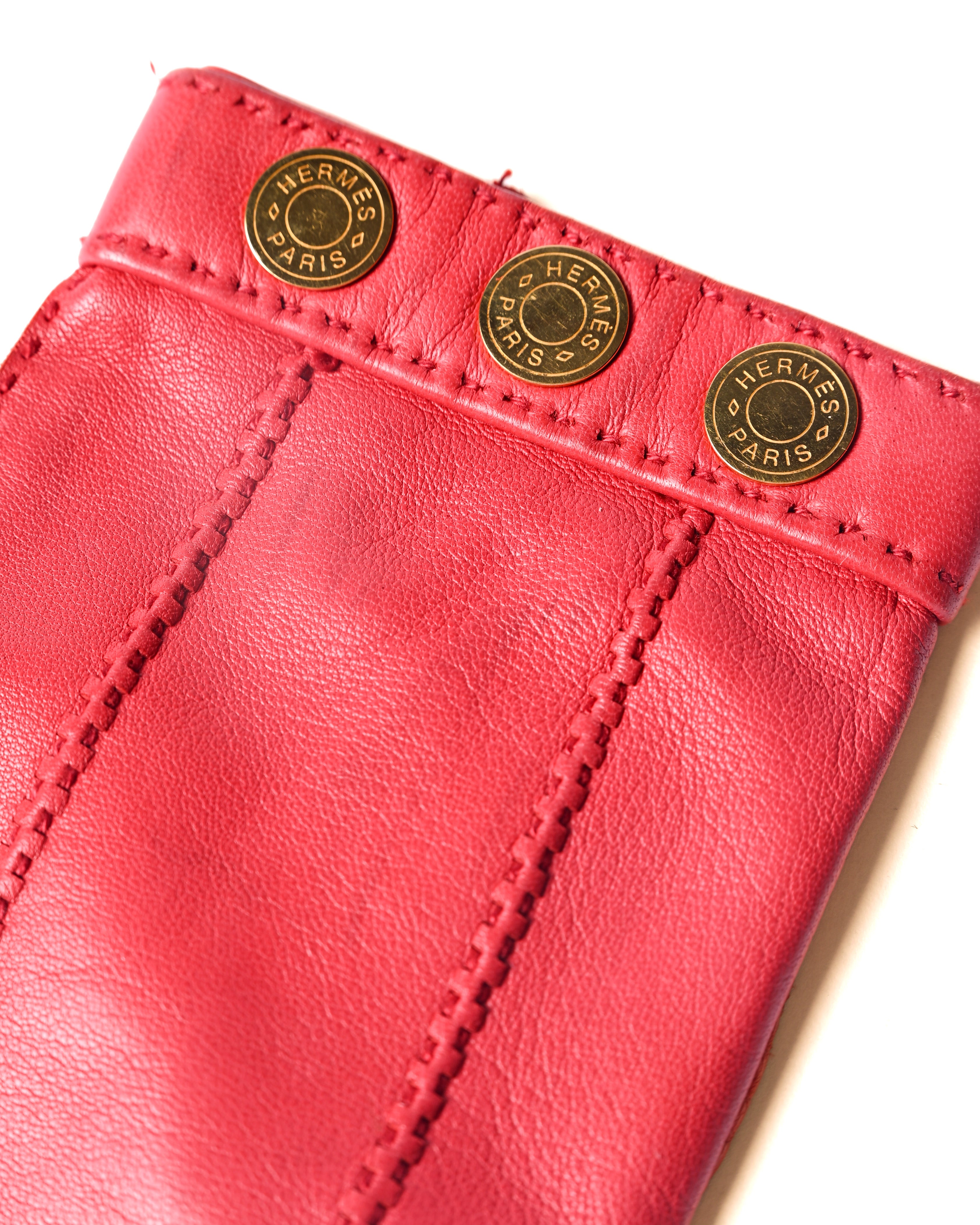 手首に3つ並ぶ、HERMES PARISの刻印入りゴールドのセリエボタンを捉えたディテールカット。鮮烈なレッドレザーと、手の甲に施されたステッチワークも確認できます。
