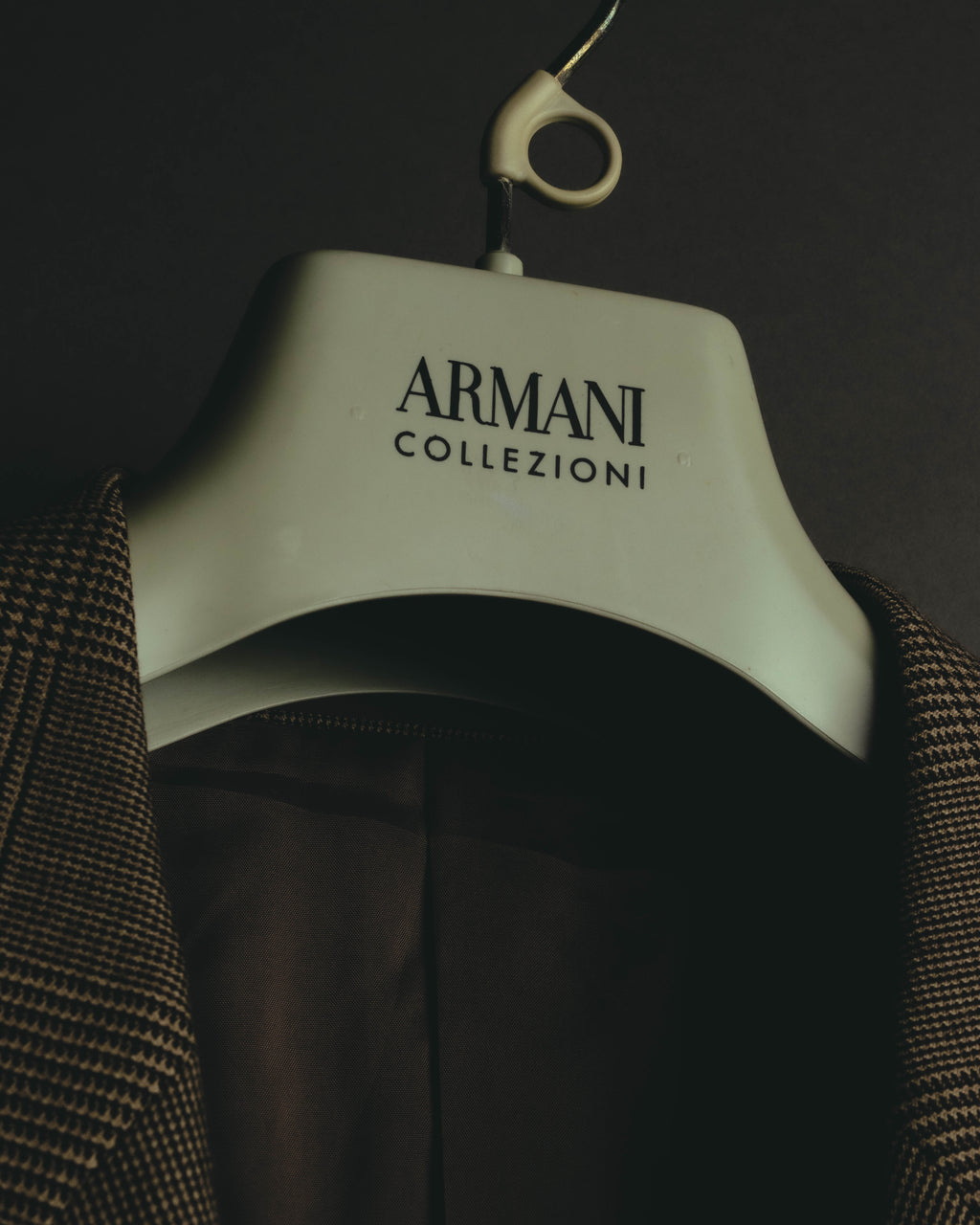 ARMANI COLLEZIONIのロゴ入りハンガーを中心に、グレンチェックの表地と落ち着いたブラウンのビスコース系裏地を捉えたカット。総裏仕様の内側の色調が確認できます。
