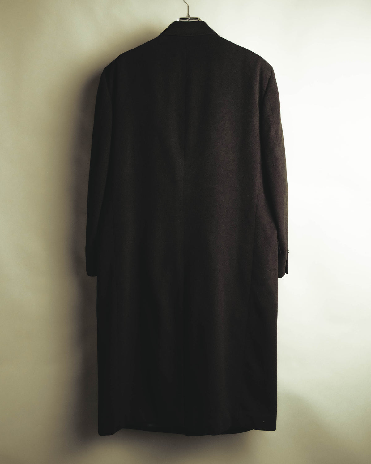 背面からロング丈と縦に流れる直線的なシルエットを確認できる全体カット。肩周りの適度な構築性と、黒に近い深色の表地が写されています。