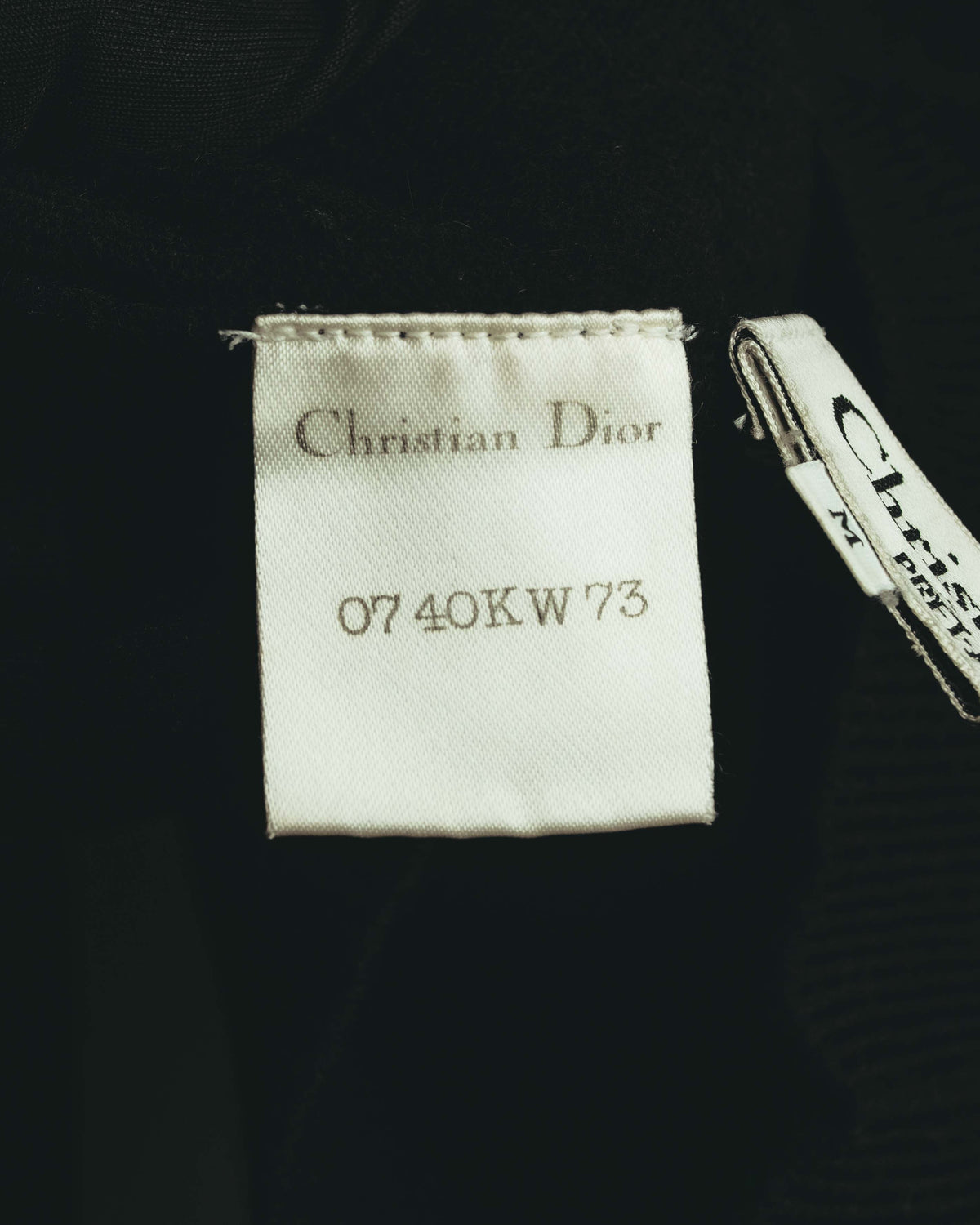 ブラックのニット内側に配されたChristian Dior表記の織りネームと、品番「0740KW73」が読めるタグのクローズアップ。横にはMサイズ表記が見える品質表示タグが付属しています。