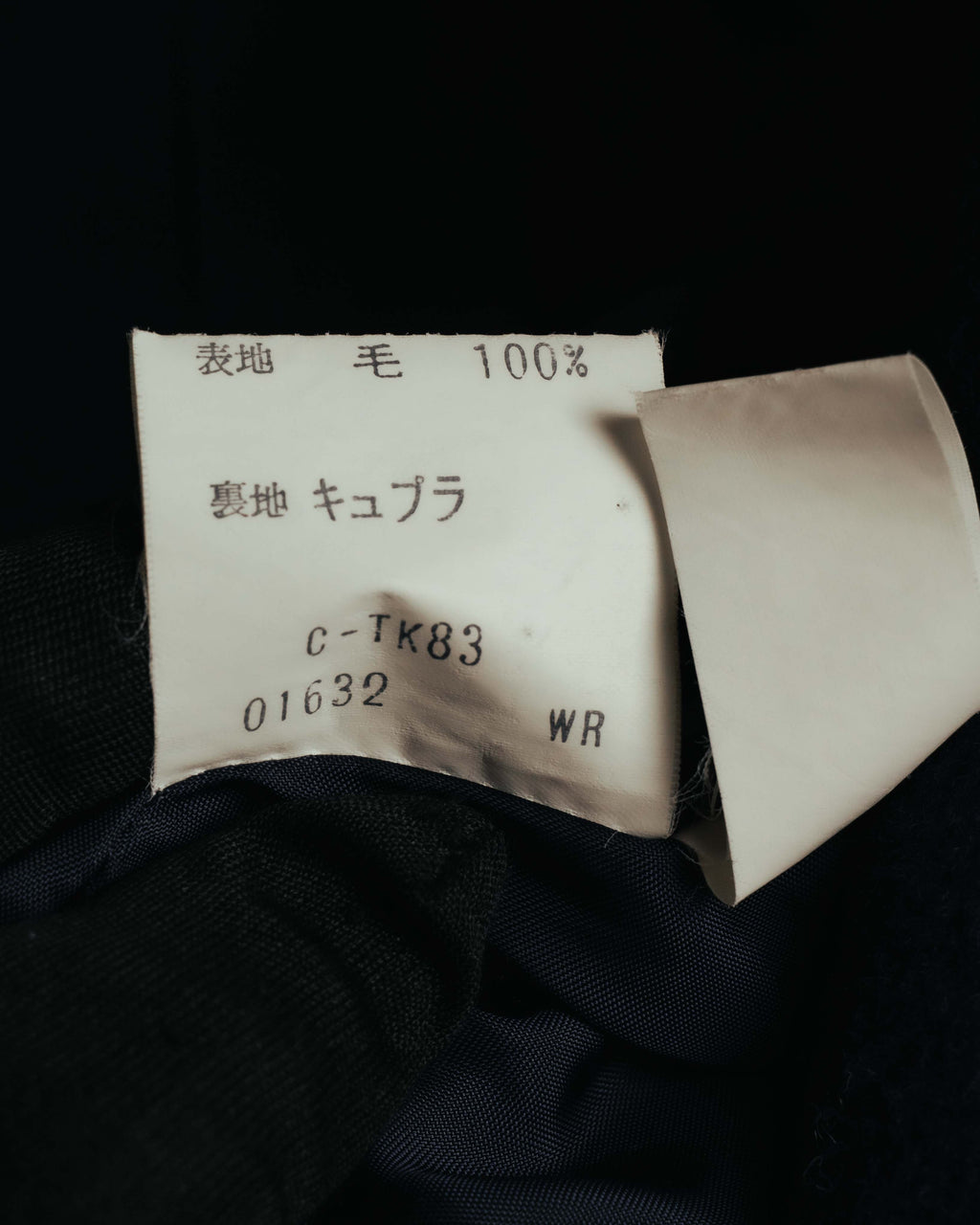 表地「毛 100%」と裏地「キュプラ」、製品コードが記載された日本語の品質表示タグ。総裏仕立ての内側に残る旧式の表記を確認できるカットです。