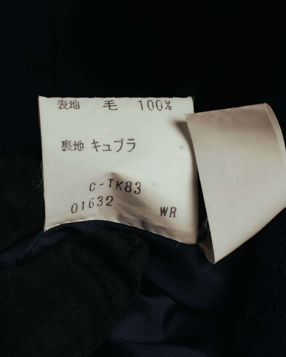 表地「毛 100%」と裏地「キュプラ」、製品コードが記載された日本語の品質表示タグ。総裏仕立ての内側に残る旧式の表記を確認できるカットです。
