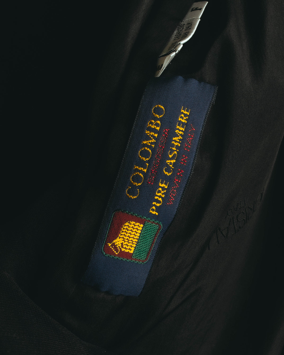 内側に配されたCOLOMBO「SPECIALISSIMA」「PURE CASHMERE」「WOVEN IN ITALY」表記の生地ネーム。イタリア製ピュアカシミヤ生地を示すタグのクローズアップ。