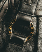 ダブルハンドルの付け根にあしらわれた、BVLGARIの刻印を反復したゴールドカラーのリング金具のディテールカット。ブラックのシボ状レザーと金具のコントラストが確認できます。