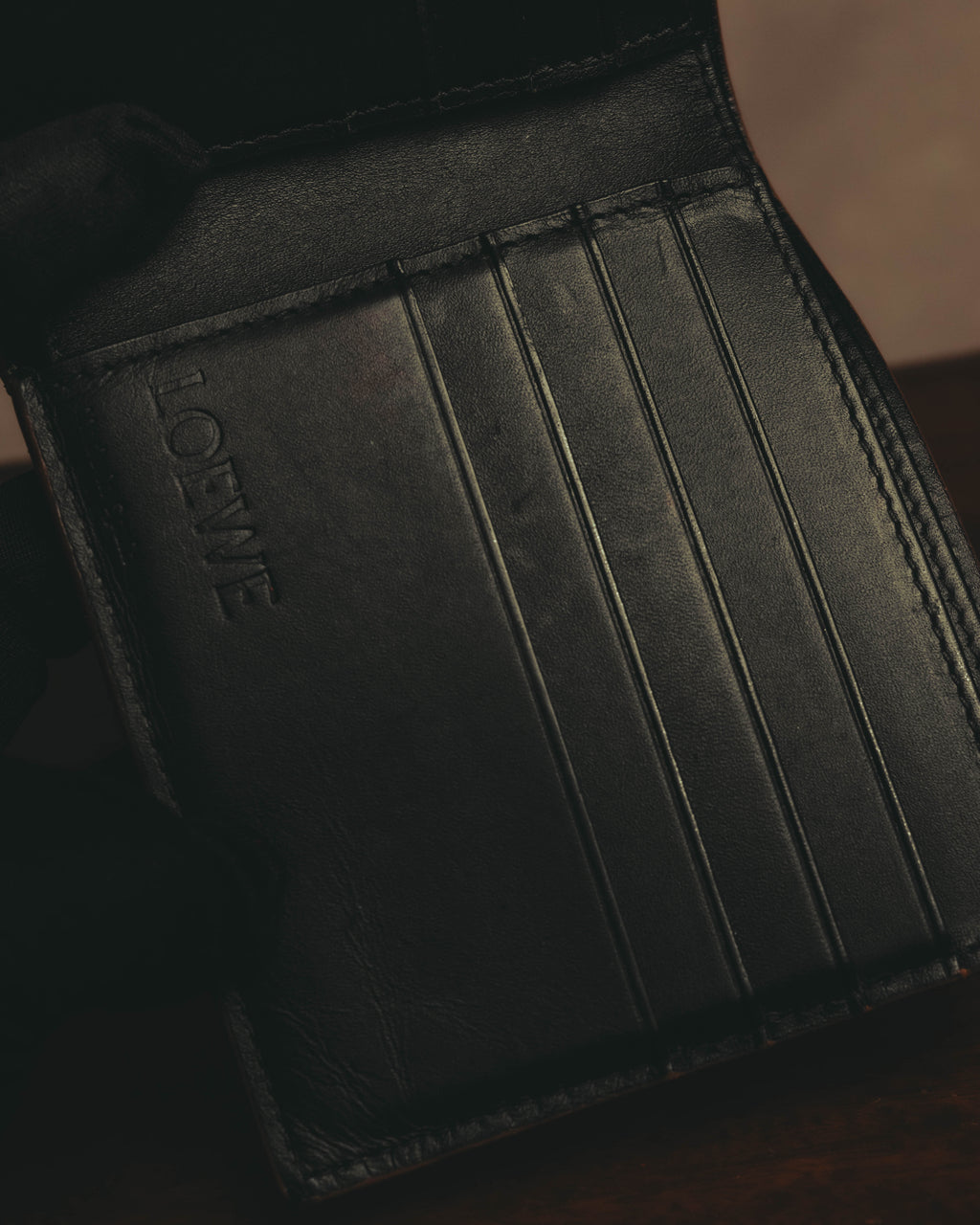 ブラックレザーの内装に並ぶカードスロットと、左側に配されたLOEWEのセリフ体ワードマークを捉えたディテールカット。カード収納部の縁にはステッチが施されています。
