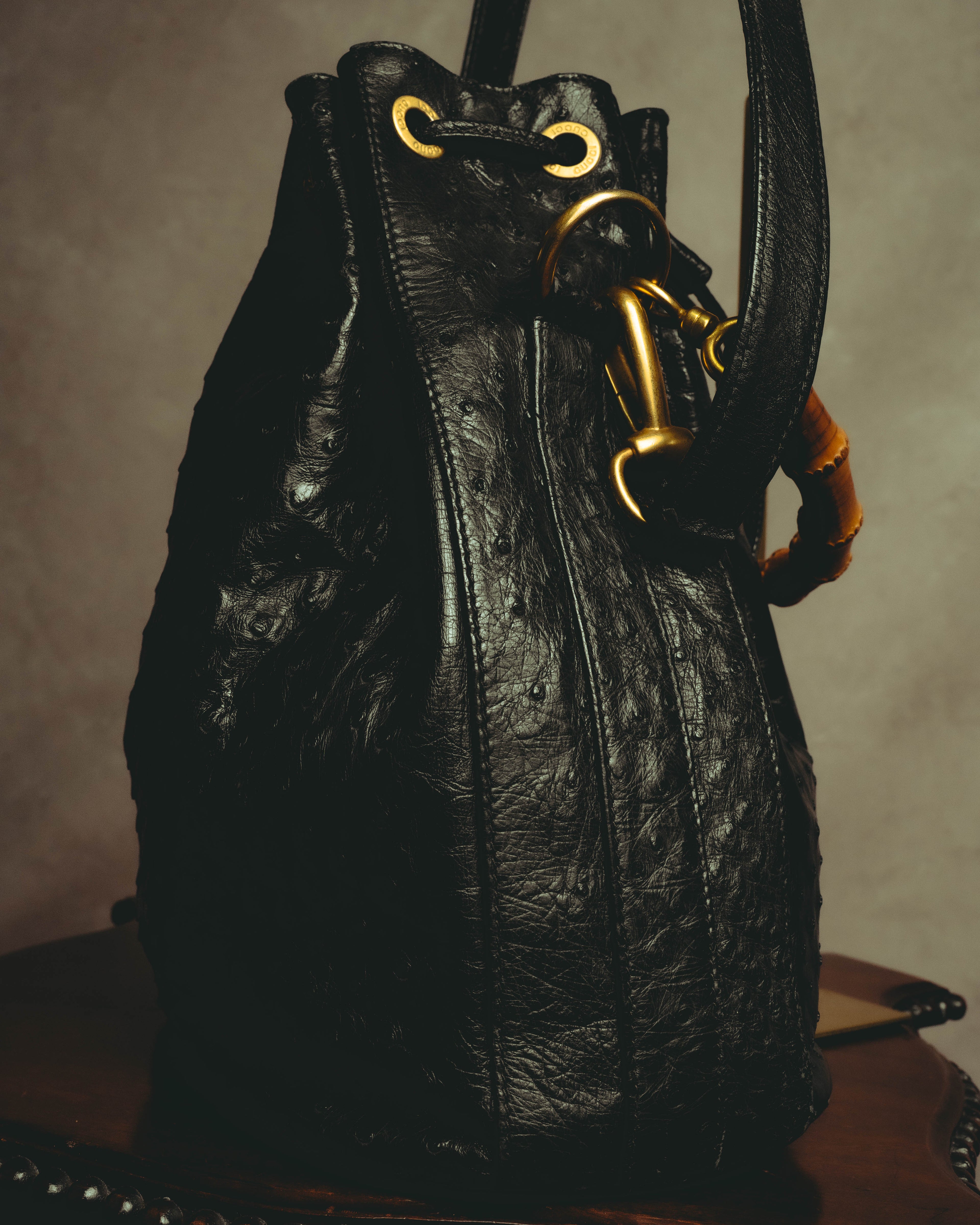 開口部に配された円周状の刻印入りアイレットと、レザー製ドローストリングを捉えたディテールカット。側面にはショルダーストラップのリング接続部と、バンブーハンドルの一部が写ります。
