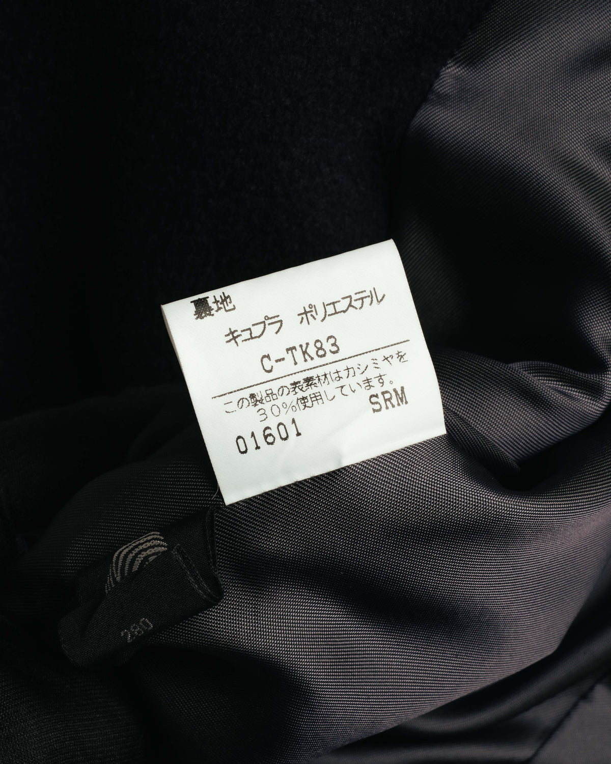 裏地に付く品質表示タグのクローズアップ。キュプラ・ポリエステルの裏地と、カシミヤ30%使用の表記が確認できるカット。