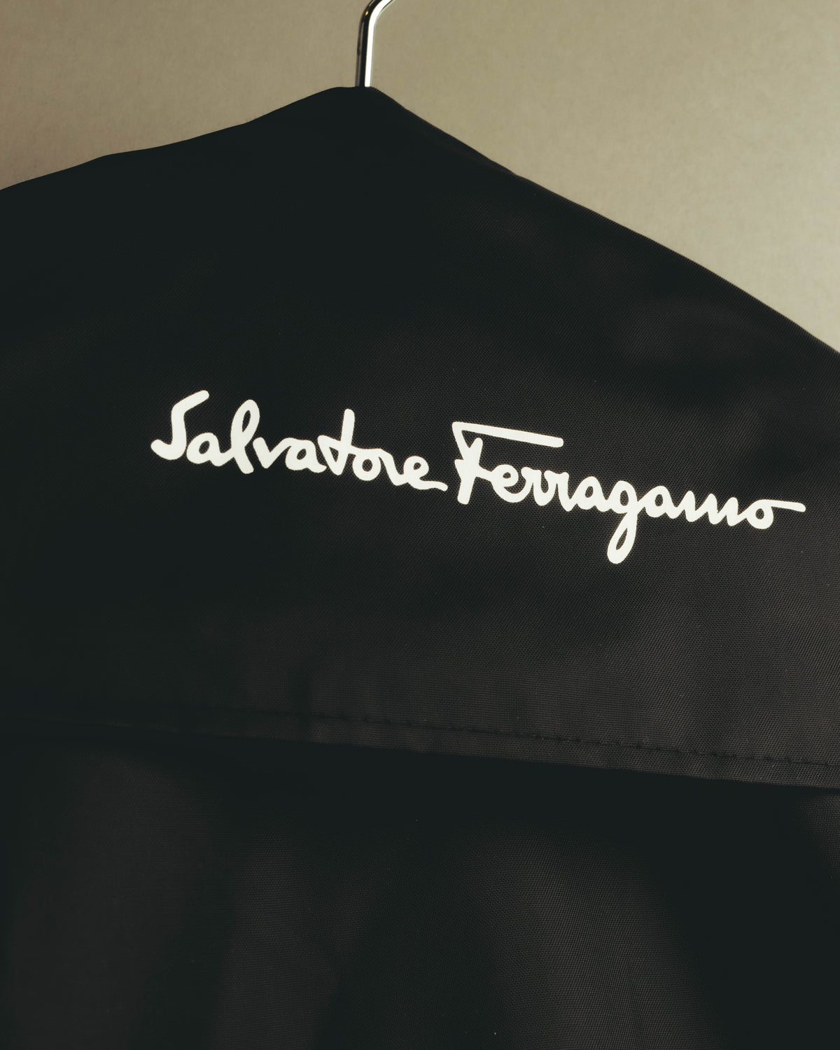 旧署名体の「Salvatore Ferragamo」ロゴを配した、ブラックのガーメントカバーのディテールカット。セットアップに付属するカバーのロゴ仕様を確認できます。