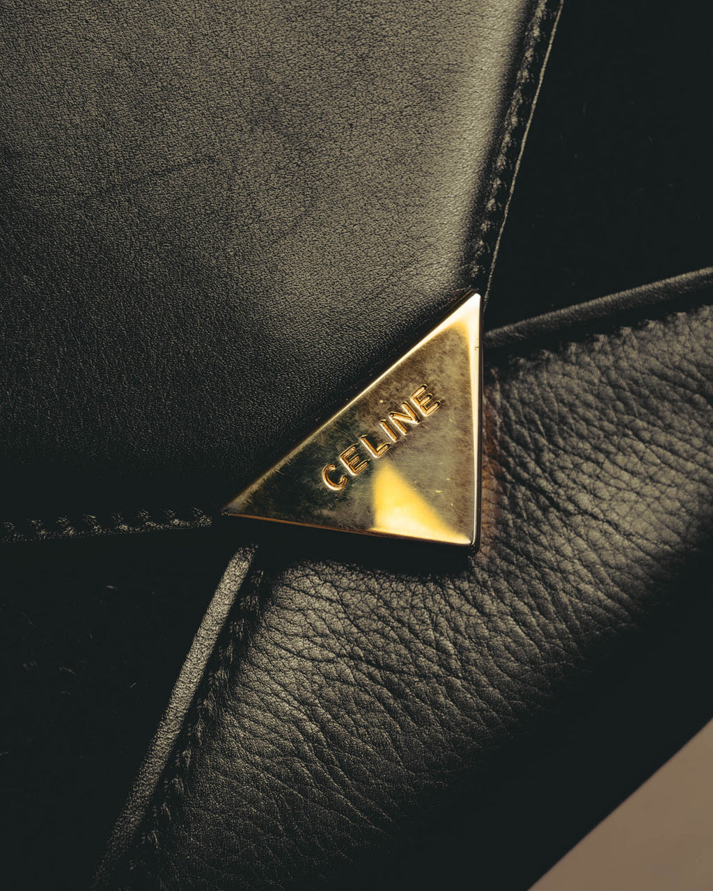 シャープな封筒型フラップに配された、CELINEの大文字刻印入り三角金具のクローズアップ。スムース調と起毛感のある質感を切り替えたフロントも確認できるディテールカット。