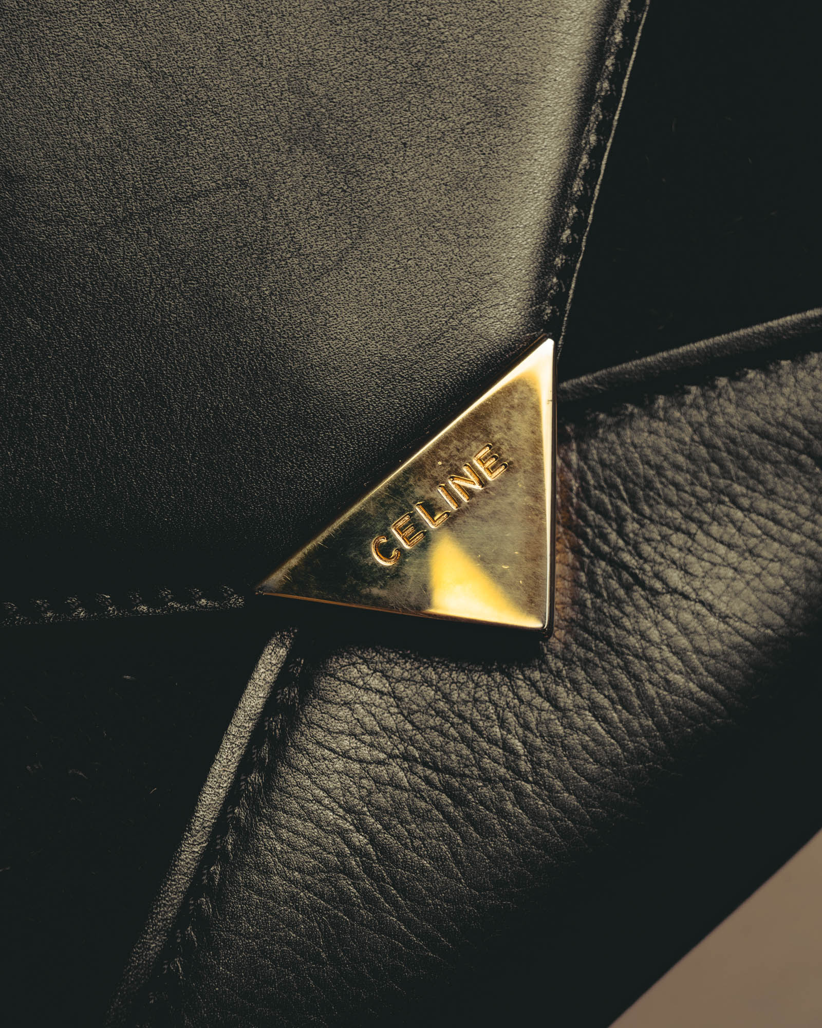 シャープな封筒型フラップに配された、CELINEの大文字刻印入り三角金具のクローズアップ。スムース調と起毛感のある質感を切り替えたフロントも確認できるディテールカット。