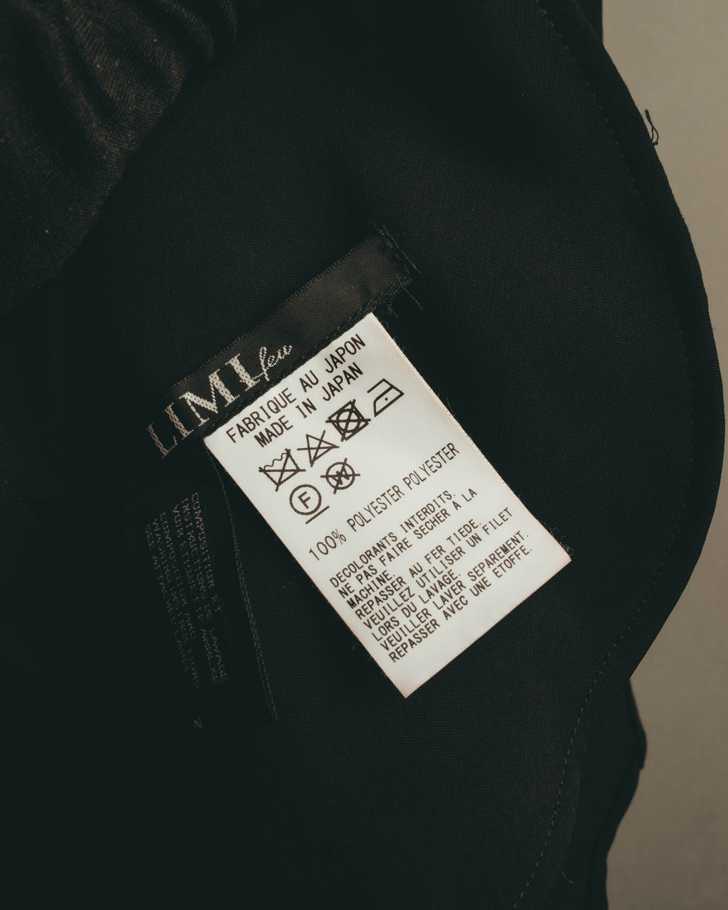 LIMI feu表記の内タグと洗濯表示を写したカット。タグ上で日本製およびポリエステル100%の素材表記が確認できます。
