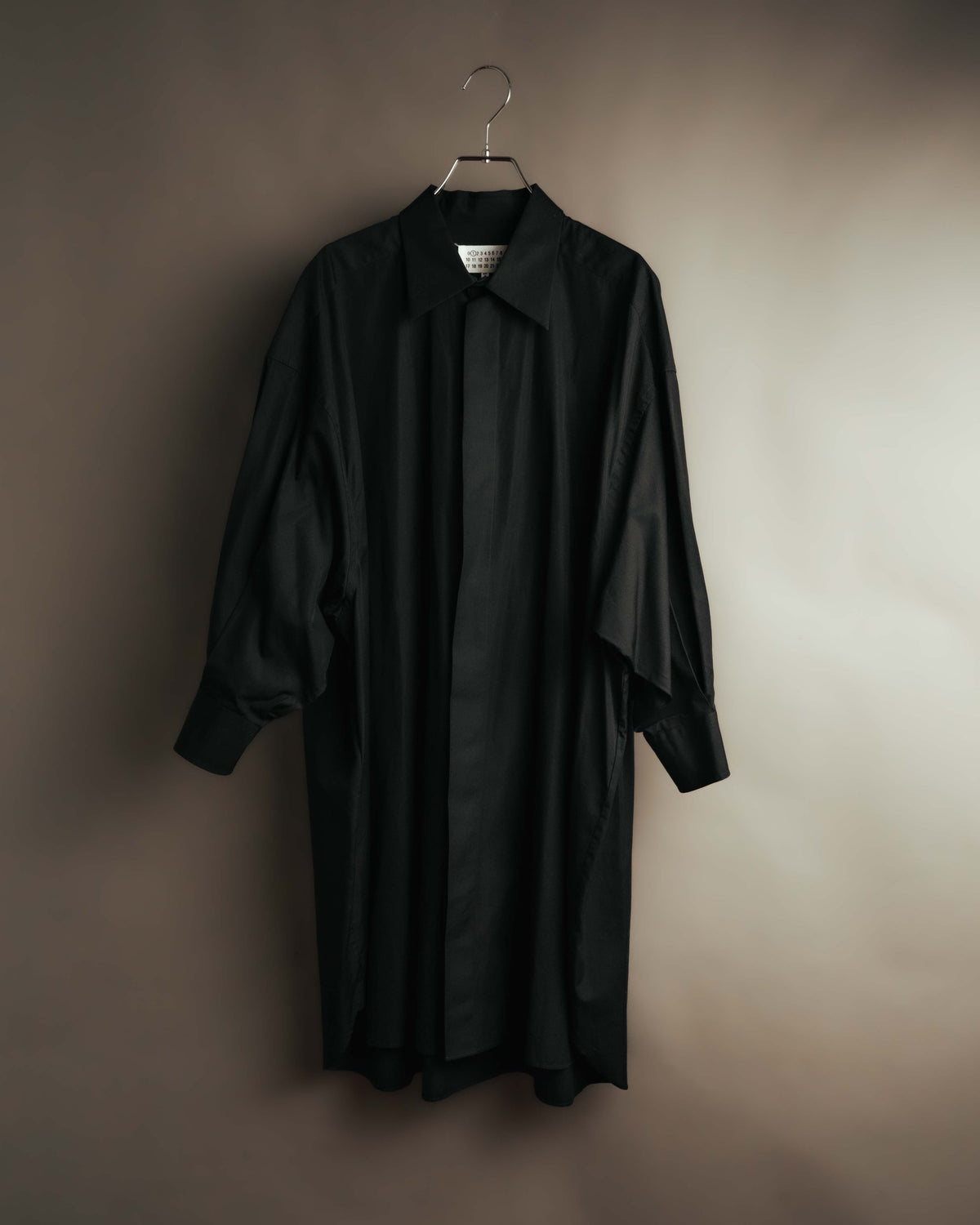 ブラックのロングシャツドレスを正面から捉えた全体像。シャープなシャツカラー、落とした肩線、ゆとりのある身幅と長いカフスのバランスが確認できるカット。