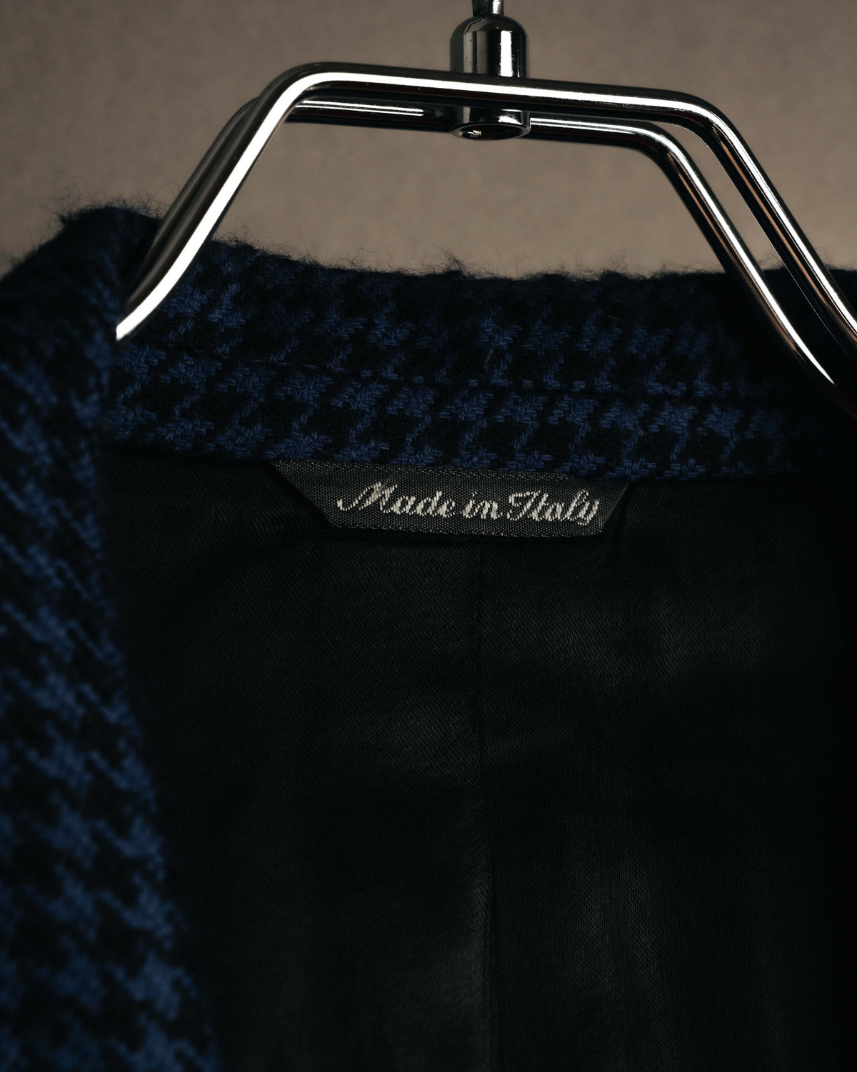 白地にアウトライン書体のVERSUSと筆記体のGianni Versaceを組み合わせた織りタグのクローズアップ。濃紺ベースの細かな千鳥格子と総裏仕立ての内側も確認できます。