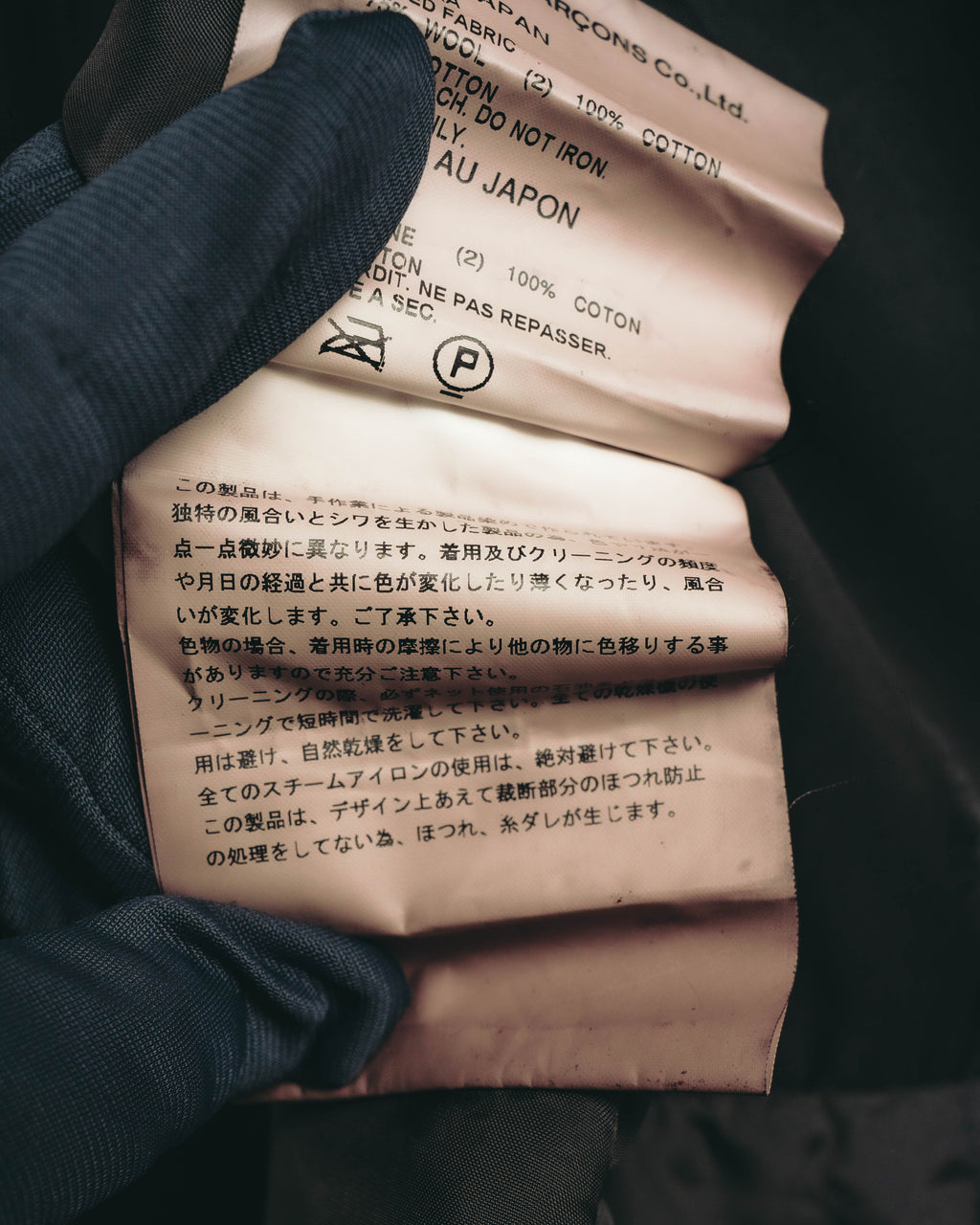 素材表記とケア表記が確認できる内側の洗濯表示タグ。裁ち切り部分のほつれや糸切れが生じる旨を記載した注意書きも写るカット。