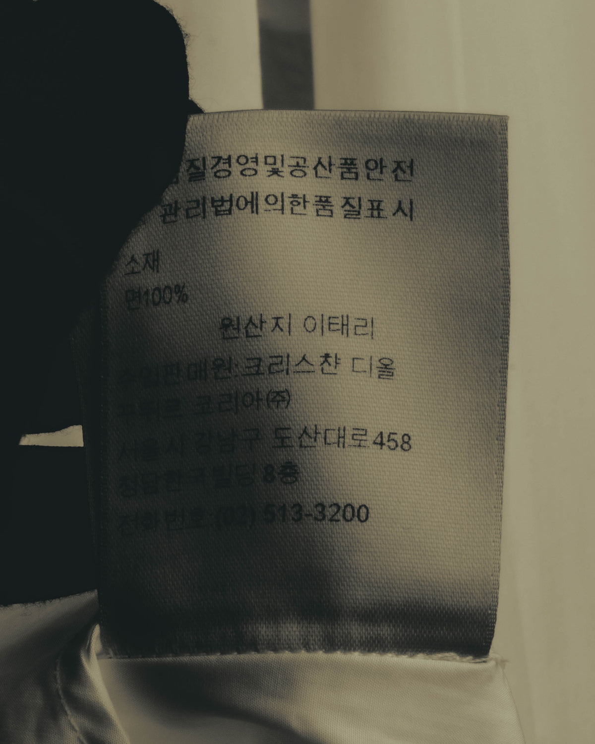 韓国語表記の品質表示タグを写したカット。素材コットン100パーセントおよび原産地イタリアの記載を確認できます。