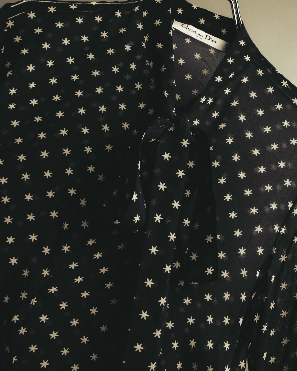 ブラックを基調にアイボリーからグレー系のスターモチーフを全面に配した、首元の細身のボウタイを捉えたディテールカット。ボウタイは柔らかく結ばれ、襟元内側のブランドタグも確認できます。