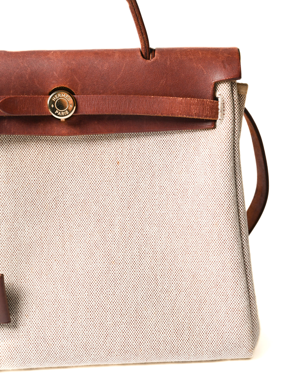 フロントのHERMÈS PARIS刻印入りゴールドカラーのセリエ金具と、ベルトを通す留め具（クラスプ）を捉えたディテールカット。生成りからライトベージュのキャンバス調織地と深いブラウンレザーの対比も確認できます。