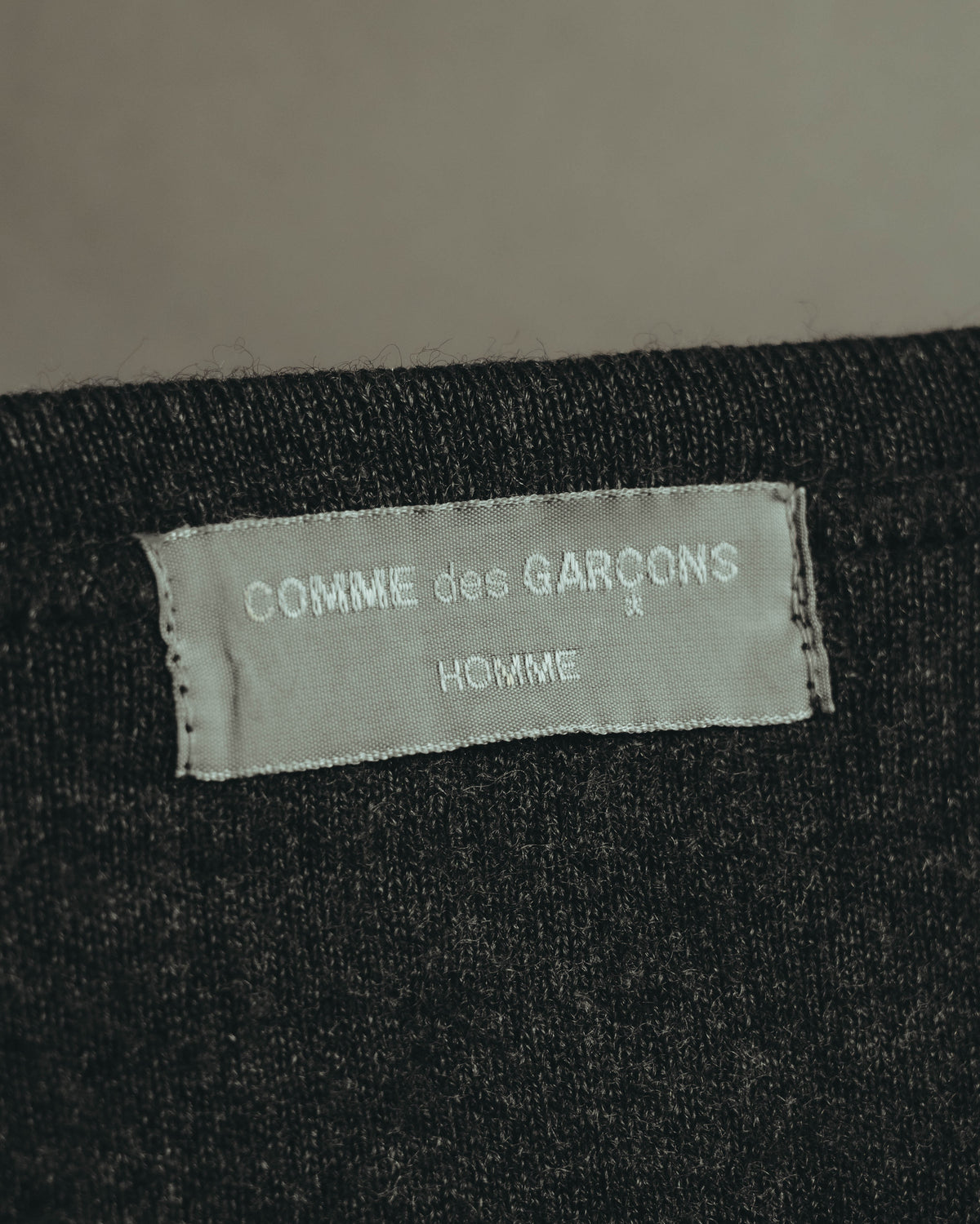 チャコールグレーのクルーネック内側に配されたブランドタグ。COMME des GARÇONS HOMMEの表記が確認できるカットです。