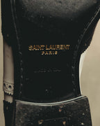 内側のインソールに、ゴールドカラーでSAINT LAURENT PARISのロゴが入るディテールカット。ブラックレザーの履き口まわりと、サイドに連なるブローギングも確認できます。