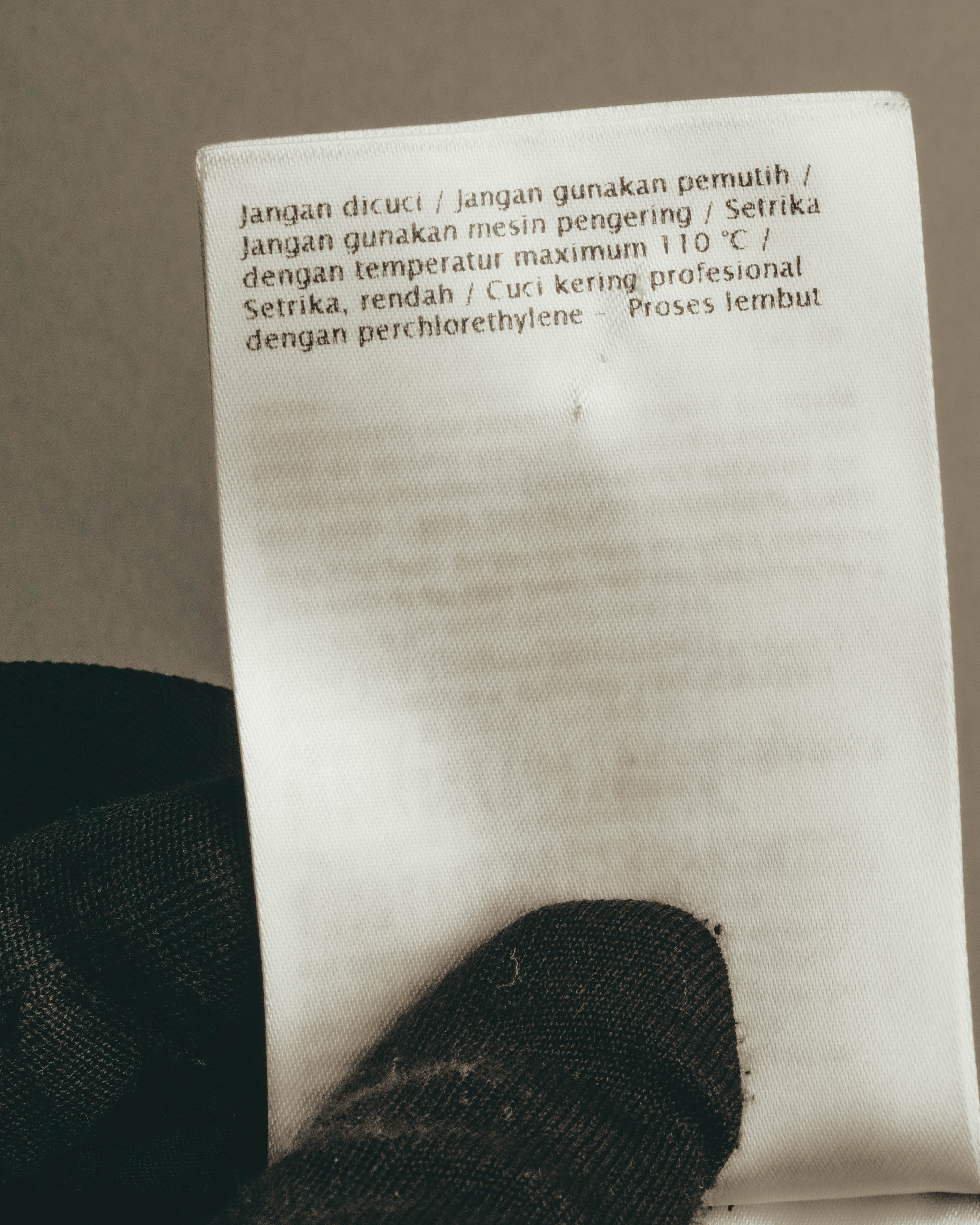 インドネシア語でケア方法が記載された洗濯表示タグのカット。漂白不可、乾燥機不可、110℃以下の低温アイロン、パークロロエチレンによる弱いドライクリーニングの表記が確認できます。