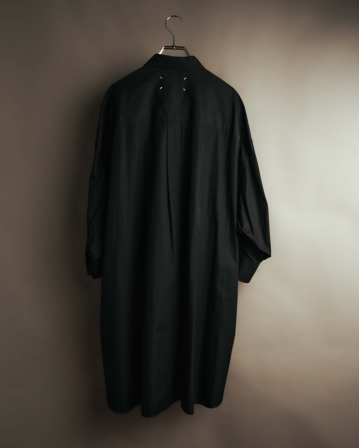 ロングシャツドレスの背面全体を捉えたカット。ネック下に配された4本の白いステッチと、裾へ流れる背面プリーツを確認できます。