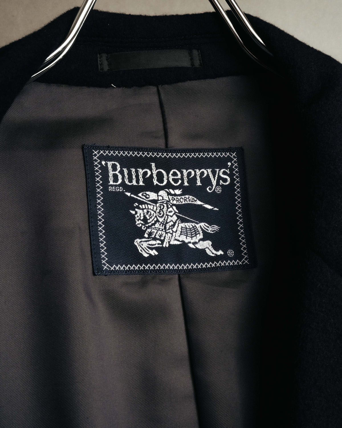 襟元の裏地に縫い付けられた、騎馬騎士図案入りの旧 Burberrys ネーム。ネーム周辺にはキュプラ・ポリエステルの裏地も確認できます。