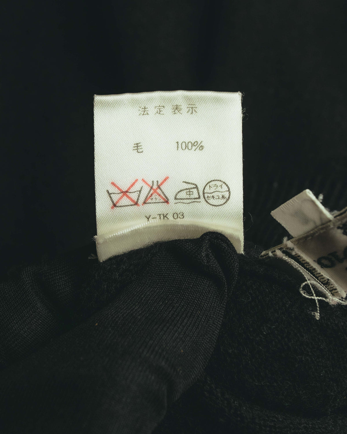 内側に配された日本語の法定表示タグ。素材表記「毛 100%」と洗濯表示を確認できるカットです。