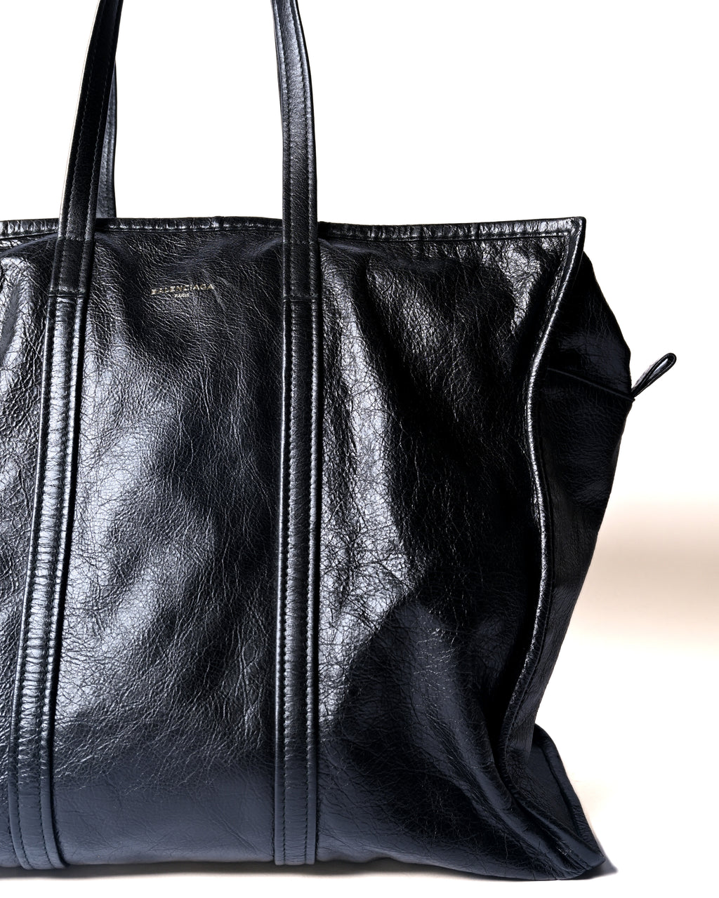 フロント上部の「BALENCIAGA PARIS」箔押しロゴと、縦に配したトップハンドルを捉えたディテールカット。自然なシワ感と程よい光沢を備えたブラックレザー、補強されたストライプ状のレザー切り替えが確認できます。